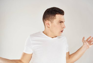 Beyaz tişörtlü bir adam, elleri arka planda açık bir şekilde el kol hareketi yapar.