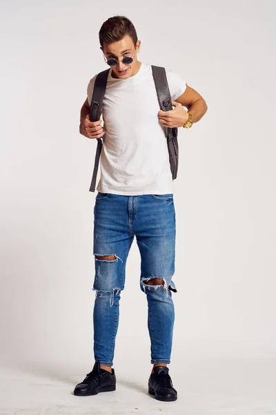 Un hombre con una mochila en la espalda en pantalones vaqueros zapatillas de deporte de longitud completa y gafas en la cara — Foto de Stock