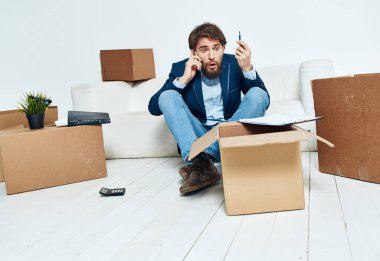 Kutuların yanındaki işadamı eşyaların açıldığı yeni bir ofise taşınıyor. 