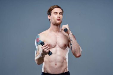 Çıplak adam gri arka planda spor yapıyor ve dambıl dövmesi kırpılmış görünüm