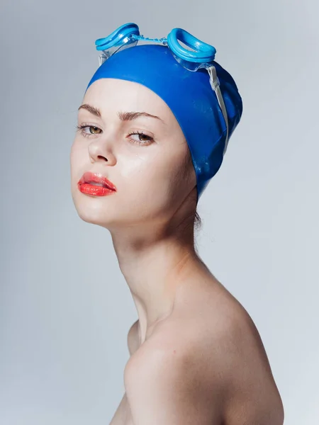 Portrait of a woman swimmer in a blue cap and glasses on the head bared shoulders