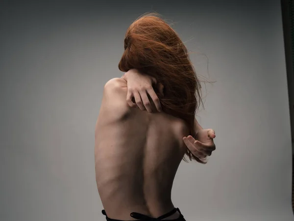 Обнажённая женщина прикасается к себе за спиной стрессовыми эмоциями рук, рыжие волосы — стоковое фото