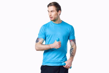 Kolunda mavi tişörtlü ve kaslı vücut geliştirme formundaki dövmeli bir adam.