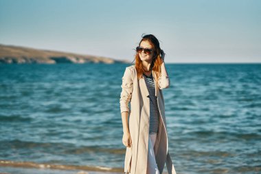 Kadın ceketli ve çizgili tişörtlü plaj dalgaları manzaralı dağlarda