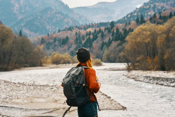 Mujer en suéter con una mochila de descanso en las montañas cerca del río en otoño en la naturaleza y árboles altos modelo —  Fotos de Stock
