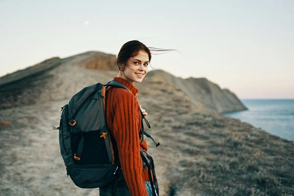 Donna felice con uno zaino cammina lungo un sentiero in montagna vicino al mare nella natura aria fresca — Foto Stock