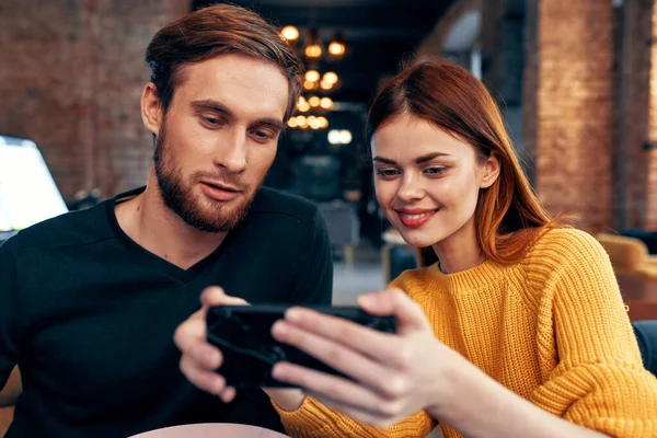 Pareja joven hombre y mujer en un restaurante pidiendo comida y teléfono móvil en la iluminación de la mano —  Fotos de Stock