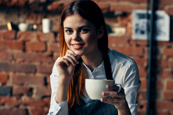Csinos nő pincér csésze ital kávézó tégla fal — Stock Fotó