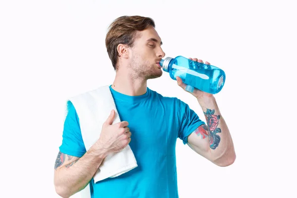 Chico deportivo en camiseta azul con una botella de agua en el río y tatuaje fondo blanco modelo fitness —  Fotos de Stock