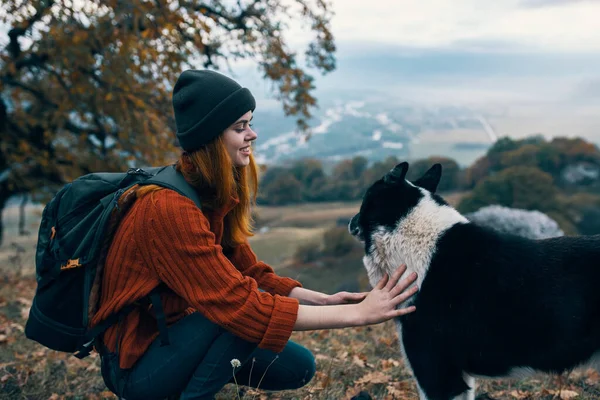 Woman with backpack in nature plays with dog in mountain landscape — Stock Photo, Image