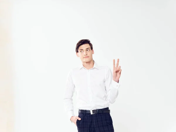 Een man in een wit shirt en zwarte broek gebaart met zijn handen op een lichte achtergrond en toont twee vingers — Stockfoto