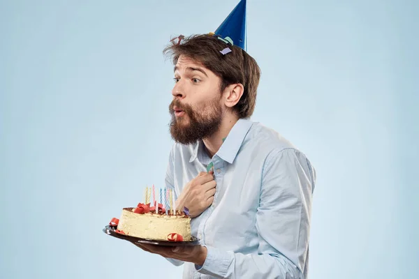 Férfi egy tál tortát, és egy ünnepi gyertya kék háttér sapka vállalati party — Stock Fotó