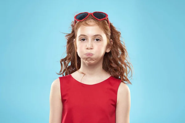 巻き毛のサングラスの赤いドレスと子供時代の楽しい青の背景を持つ女の子 — ストック写真