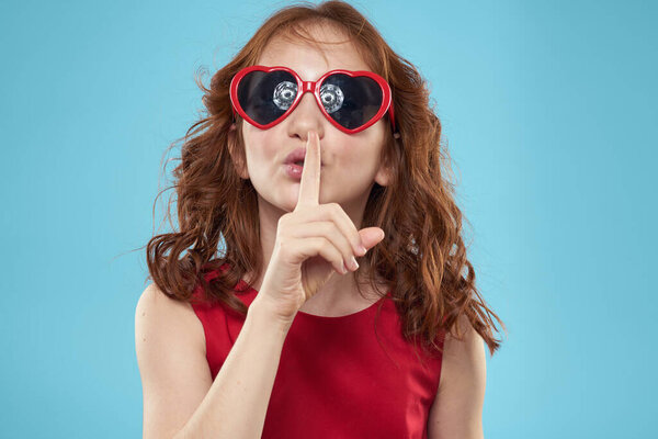 Little girl in sunglasses in the form of hearts red dress curly hair blue background