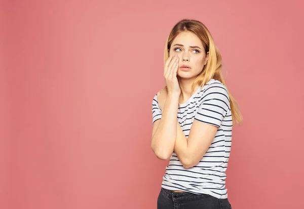 Pembe arka planda çizgili tişörtlü üzgün sarışın kadın. — Stok fotoğraf