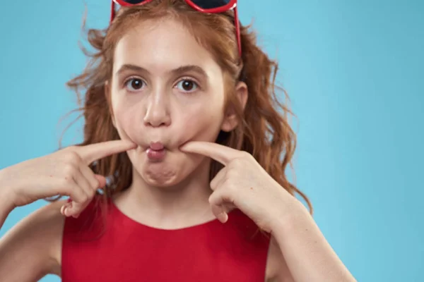 Fille avec des lunettes de soleil cheveux bouclés robe rouge et l'enfance amusant fond bleu — Photo