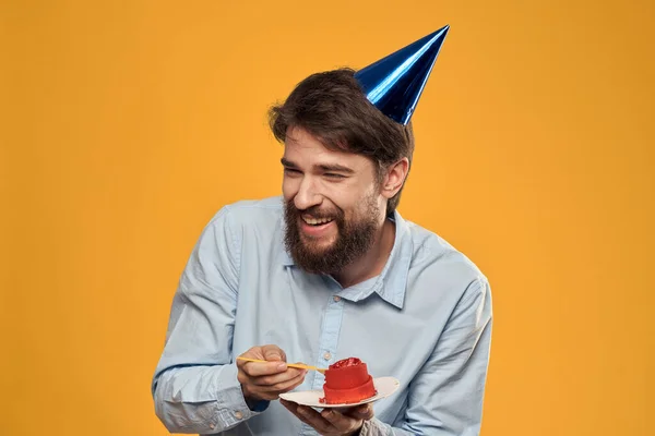 손에 생일 케이크를 쥐고 생일에 노란 배경에 모자를 쓴 남자 — 스톡 사진