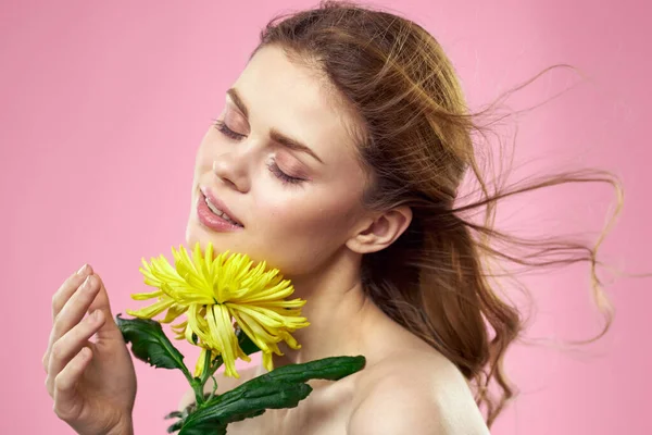 Hermosa chica con una flor amarilla sobre un fondo rosa maquillaje hombros desnudos —  Fotos de Stock