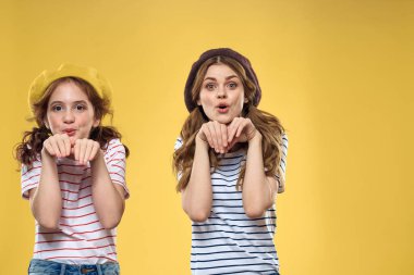 Şapkalı neşeli kız kardeşler çizgili tişörtler, neşeli yaşam tarzı sarı arka plan ailesi