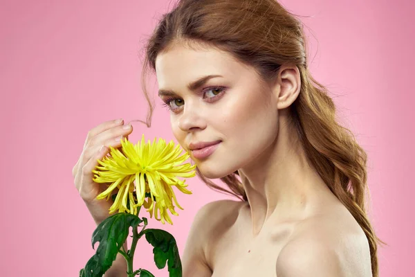 Porträtt av en kvinna med gula blommor på en rosa bakgrund Makeup i ansiktet — Stockfoto