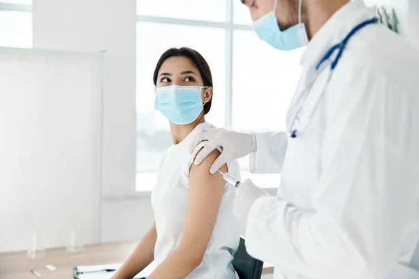 의료용 가운을 입은 의사가 의료용 마스크를 쓴 환자의 어깨에 백신을 주사한다 — 스톡 사진