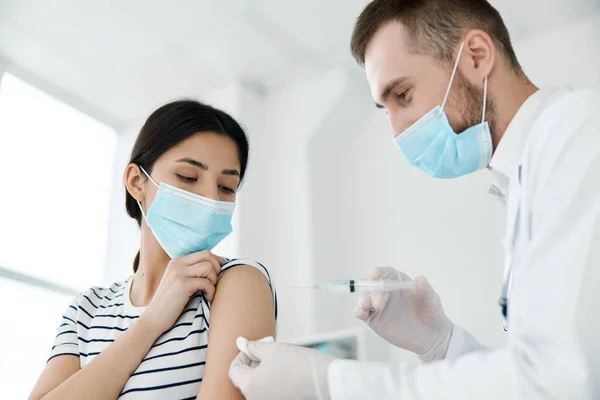 En läkare injicerar ett vaccin till en kvinnlig patient i en medicinsk mask — Stockfoto