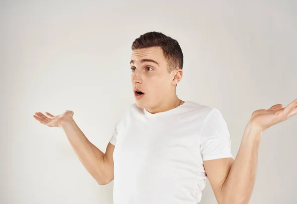A man in bewilderment gestures with his hands on a light background in a white T-shirt cropped view — Stock Photo, Image