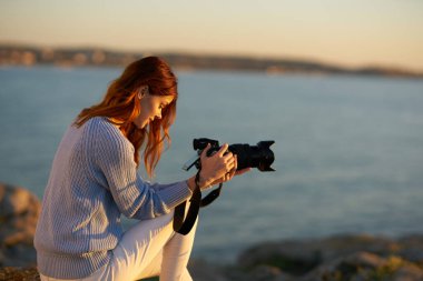 Gün batımında deniz kenarında profesyonel kameralı bir kadın.