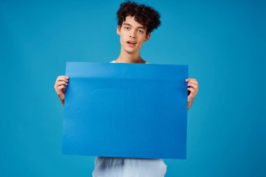 Beyaz tişörtlü bir adam elinde poster reklamı tutuyor.