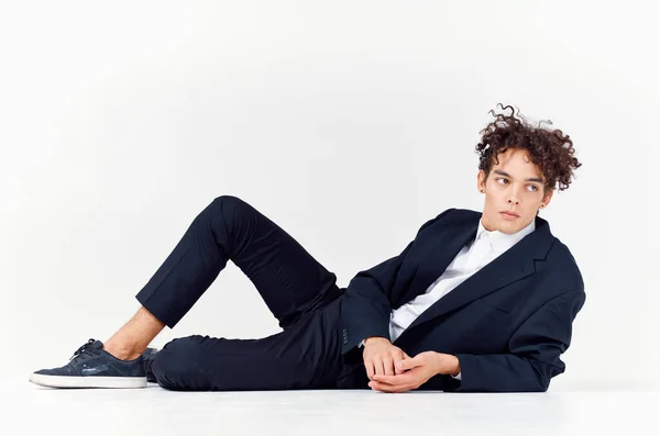 En kille en tonåring i kostym ligger på golvet och sneakers lockigt hår ljus bakgrund — Stockfoto