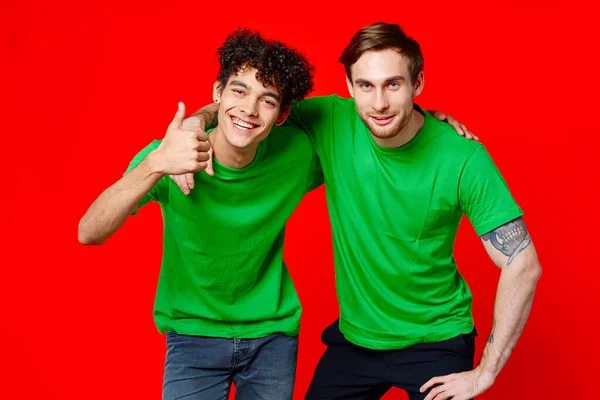 Due amici in verde t-shirt abbracci divertimento rosso sfondo — Foto Stock