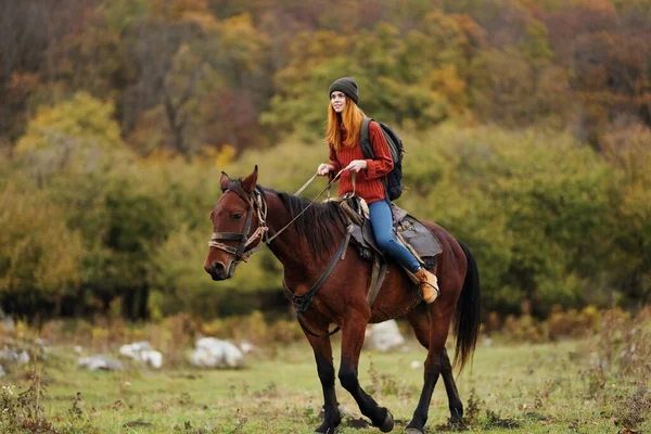 Mulher caminhante com uma mochila monta um cavalo nas montanhas natureza amizade — Fotografia de Stock