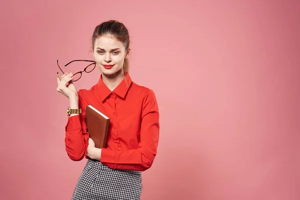 Zakelijke vrouw in een rood shirt elegante roze achtergrond met een notebook in haar handen — Stockfoto