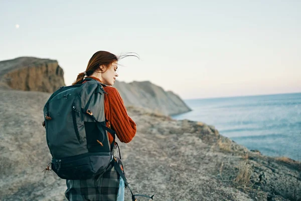 Schöne Modell mit einem Rucksack auf dem Rücken in den Bergen in der Natur in der Nähe des Meeres und hohe Felsen — Stockfoto