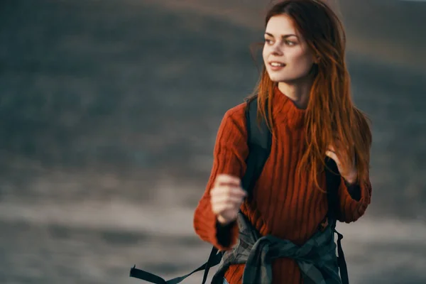 Ευτυχισμένη ταξιδιώτη σε ένα κόκκινο πουλόβερ με ένα σακίδιο στην πλάτη της στηρίζεται στα βουνά του τρόπου ζωής της φύσης — Φωτογραφία Αρχείου
