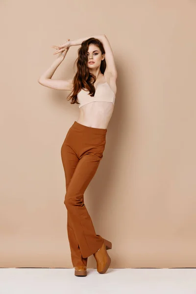 Mujer sexy en sujetador y pantalones marrones zapatos de tacón alto fondo beige gesto con las manos —  Fotos de Stock