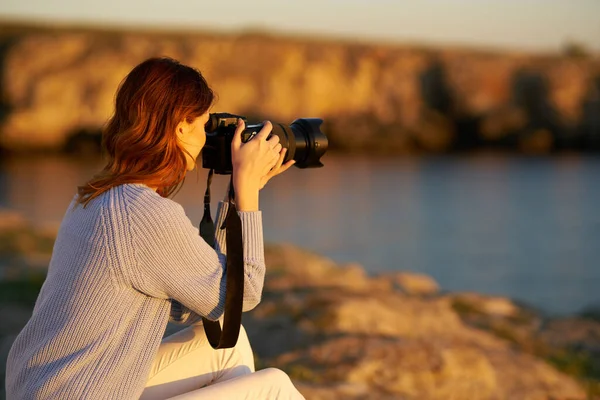 Woman in the mountains near the sea at sunset with a professional camera in her hands — Stock Photo, Image