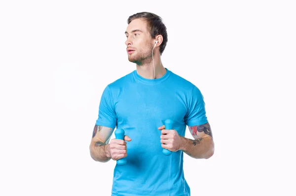 Homem com halteres em uma camiseta azul em um fundo claro olhando para o lado recortado vista — Fotografia de Stock