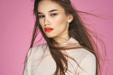 Beyaz süveter içinde güzel esmer, kırmızı dudaklı çekici pembe arka planda.