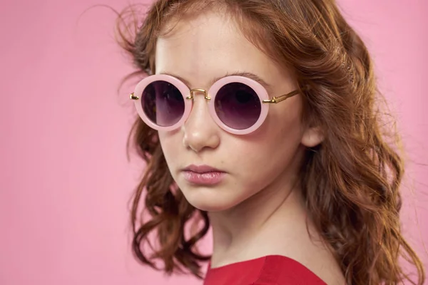 カールしたヘアサングラスを持つ女の子子供時代喜びピンクの背景 — ストック写真