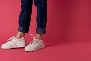 Kadın ayakları, beyaz spor ayakkabıları, sokak moda, pembe arka plan.