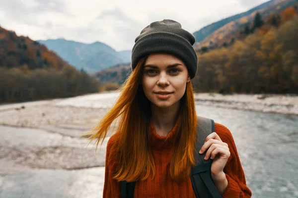 아름다운 여인 이 스웨터를 입고 강 근처에 있는 산 속에 배낭을 메고 자연 사진을 찍고 있다 — 스톡 사진