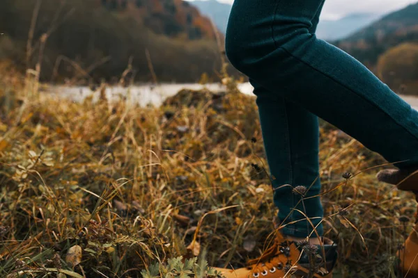 Mulheres pés jeans sapatos grama seca outono rio montanhas à distância — Fotografia de Stock