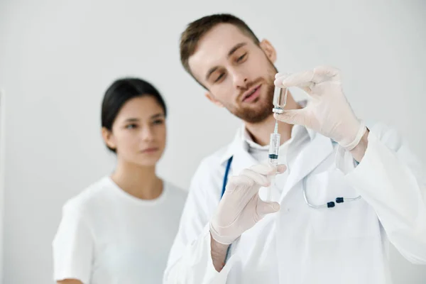 Male doctor with a syringe in his hand and a female patient in the background vaccination — Stock Photo, Image