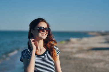 Gözlüklü, kızıl saçlı, plaj manzaralı güzel bir gezginin portresi.