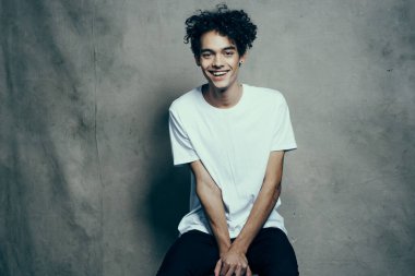 Tişörtlü mutlu kıvırcık adam. Stüdyo fotoshoot modelinin kumaş arka planında el kol hareketi yapıyor.