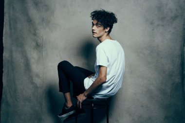 Pantolon ve tişörtlü, kıvırcık saçlı, perde arkası fotoğraf stüdyosu.