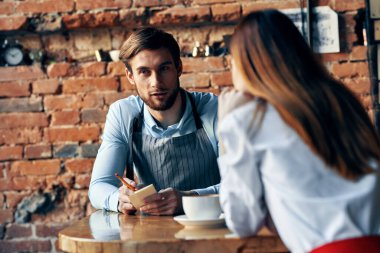 Kafe masasında bir fincan kahve ve önlüklü bir adam ve kırmızı etekli bir kadın.