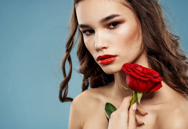 Atraktivní bruneta s červenou růží v blízkosti obličeje na modrém pozadí — Stock fotografie