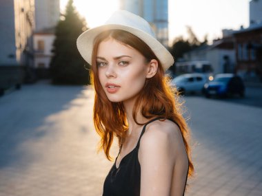 Siyah elbiseli ve beyaz şapkalı bir kadın portresi. Gün batımında binanın yanındaki sokakta.